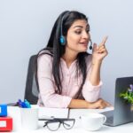 happy-young-beautiful-woman-casual-clothes-with-headphones-microphone-sitting-table-with-laptop-having-video-call-white-background-working-office-1