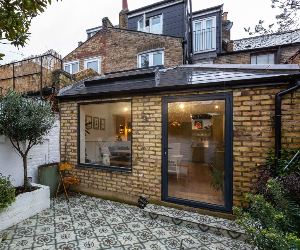 A side-return brick addition on a London terraced house featuring a large fixed picture window and a black-framed glass door, serving as a primary model for a home extension costs calculator UK.