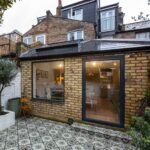 A side-return brick addition on a London terraced house featuring a large fixed picture window and a black-framed glass door, serving as a primary model for a home extension costs calculator UK.