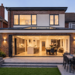 A luxury rear view of a large double-storey brick addition featuring a wide open-plan kitchen with bifold doors and integrated outdoor lighting, showcasing high-end house extensions London.
