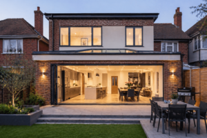 A luxury rear view of a large double-storey brick addition featuring a wide open-plan kitchen with bifold doors and integrated outdoor lighting, showcasing high-end house extensions London.