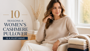 A woman in a beige cashmere pullover sitting comfortably on a chair with folded cashmere sweaters beside her, highlighting the warmth and elegance of cashmere.