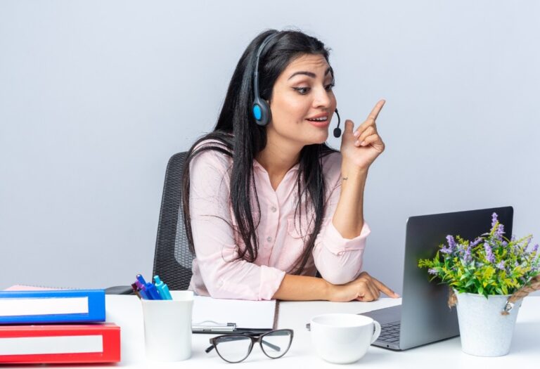 happy-young-beautiful-woman-casual-clothes-with-headphones-microphone-sitting-table-with-laptop-having-video-call-white-background-working-office-1